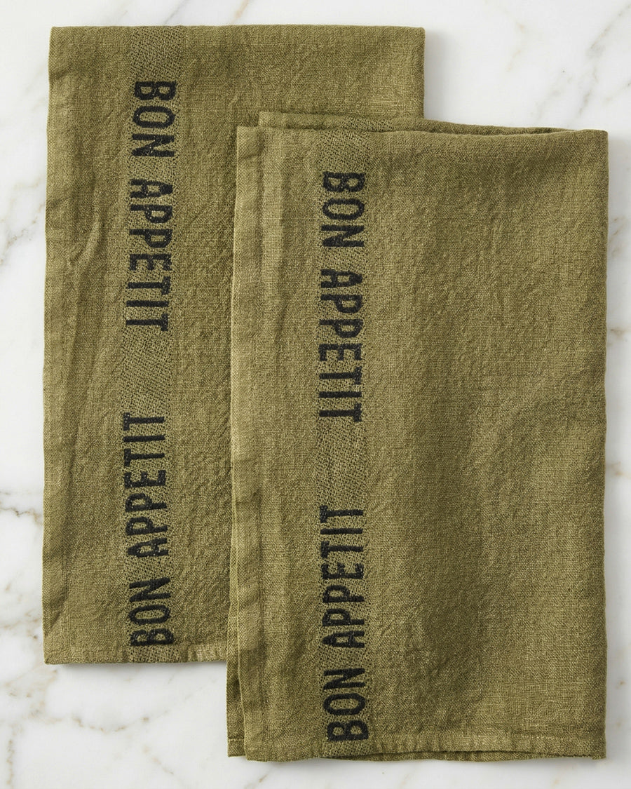 Two olive green linen towels with 'Bon Appetit' text on a marble surface, by Charvet Editions available via Wildschut Antiques.