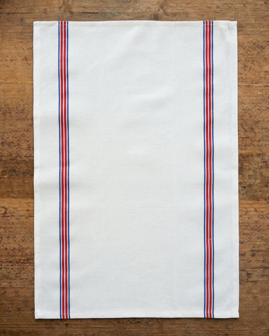 White towel with red and blue stripes on a wooden surface, by Charvet Editions available via Wildschut Antiques