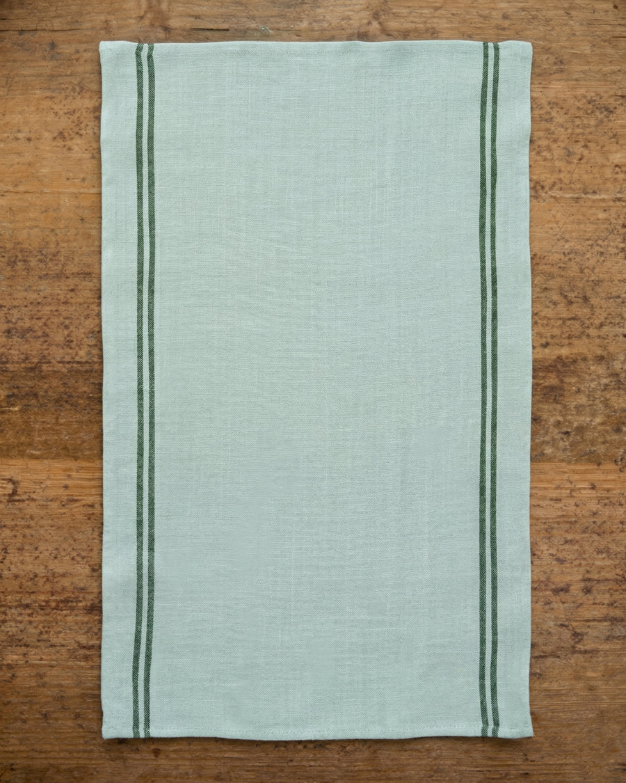 Mint green linen towel with dark stripes on a wooden surface. Linen Country Towel by Charvet Editions available via Wildschut Antiques.