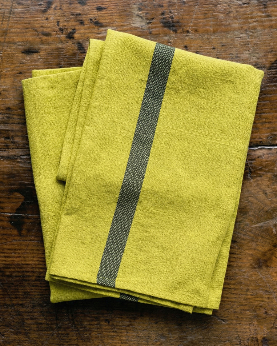 Lemon yellow linen towels with a dark stripe on a wooden surface, by Charvet Editions available via Wildschut Antiques.