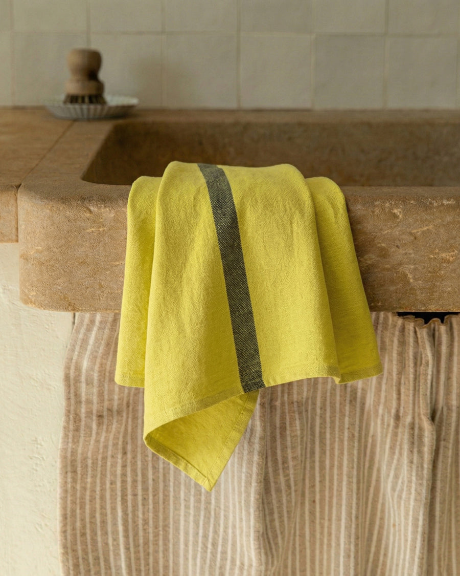 Lemon yellow linen towel with a stripe draped over a stone sink in a kitchen, by Charvet Editions available via Wildschut Antiques.