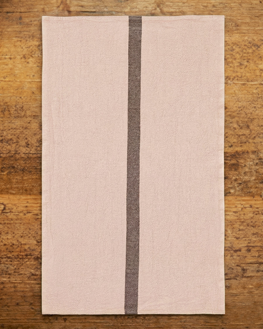Light pink towel with a dark stripe on a wooden surface, by Charvet Editions available via Wildschut Antiques.