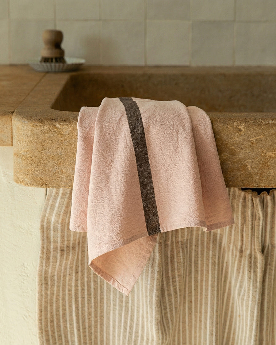 Pink linen towel draped over a stone sink in a kitchen setting, by Charvet Editions available via Wildschut Antiques.