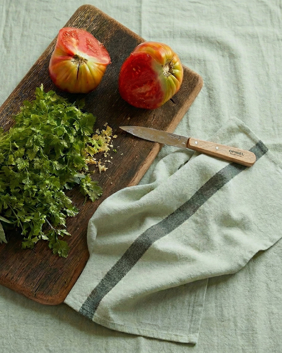 Wooden cutting board with apples, herbs, and a knife on a light green fabric background, next to a pistache green linen towel by Charvet Editions available via Wildschut Antiques.