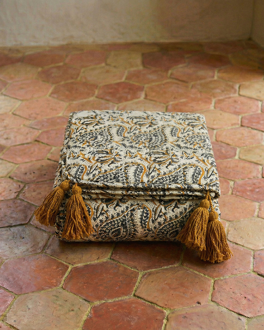 Decorative folded cotton blanket with tassels on a terracotta floor, available via Wildschut Antiques.
