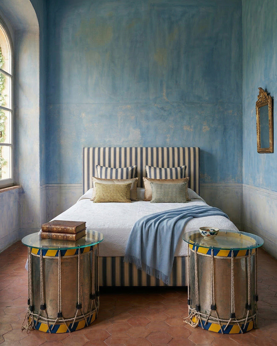 Bedroom with blue walls, striped bed, and decorative side tables in the form of vintage drums, all items available via Wildschut Antiques.