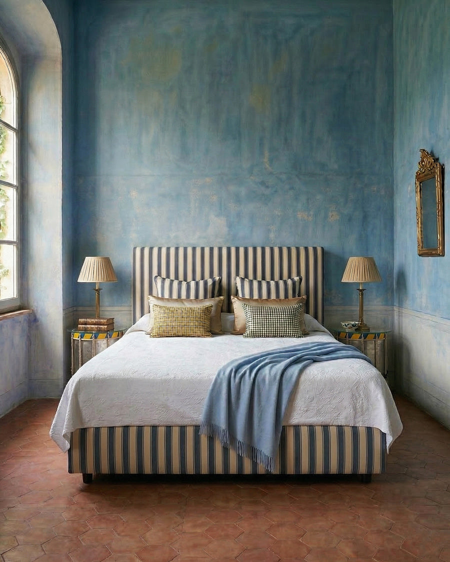 Bedroom with blue walls, striped bed, and decorative side tables in the form of vintage drums, all items available via Wildschut Antiques.