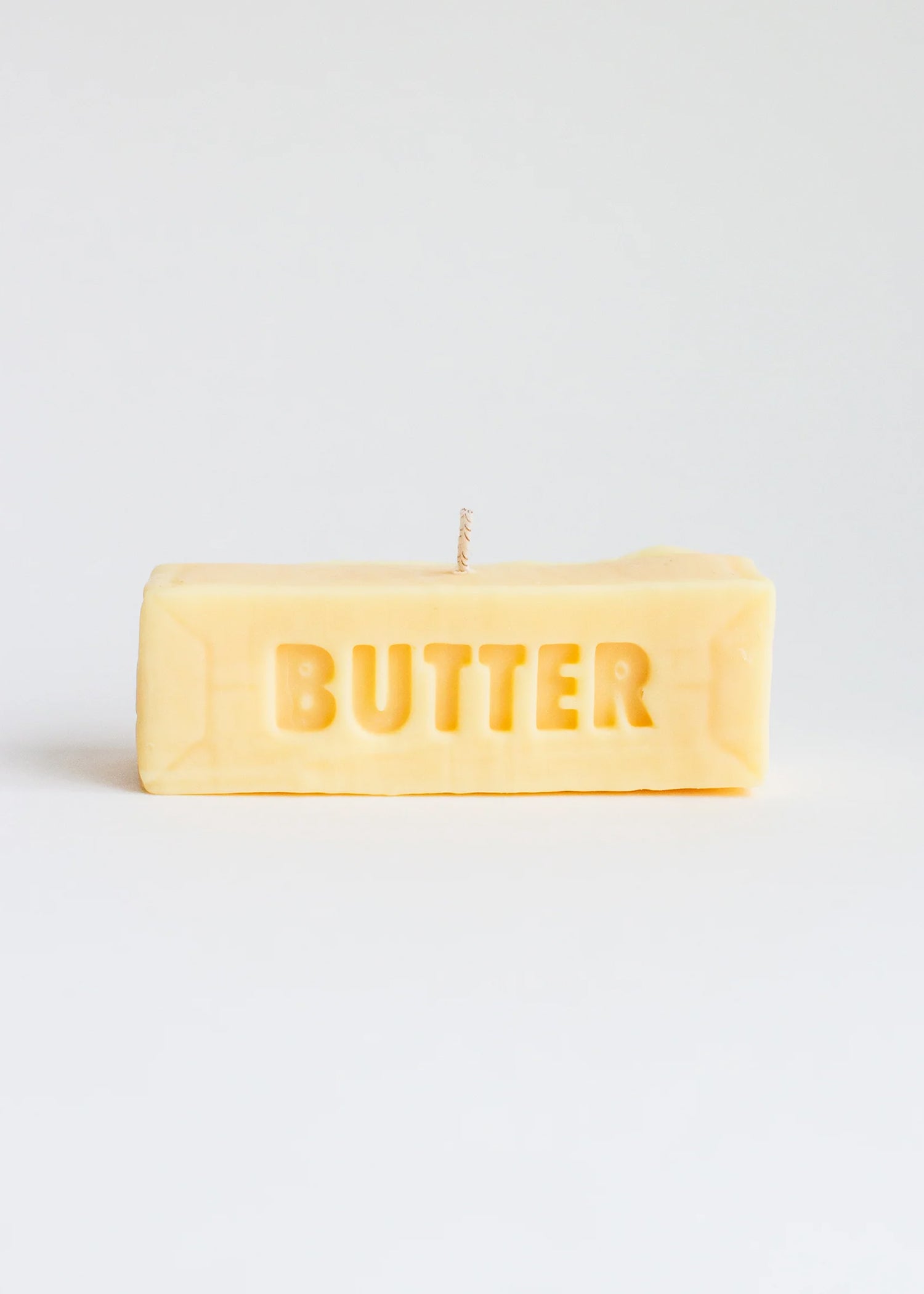 Candle in the shape of a stick of butter on a white background. Part of the Playful Food Candle Collection available via Wildschut Antiques Concept Store.