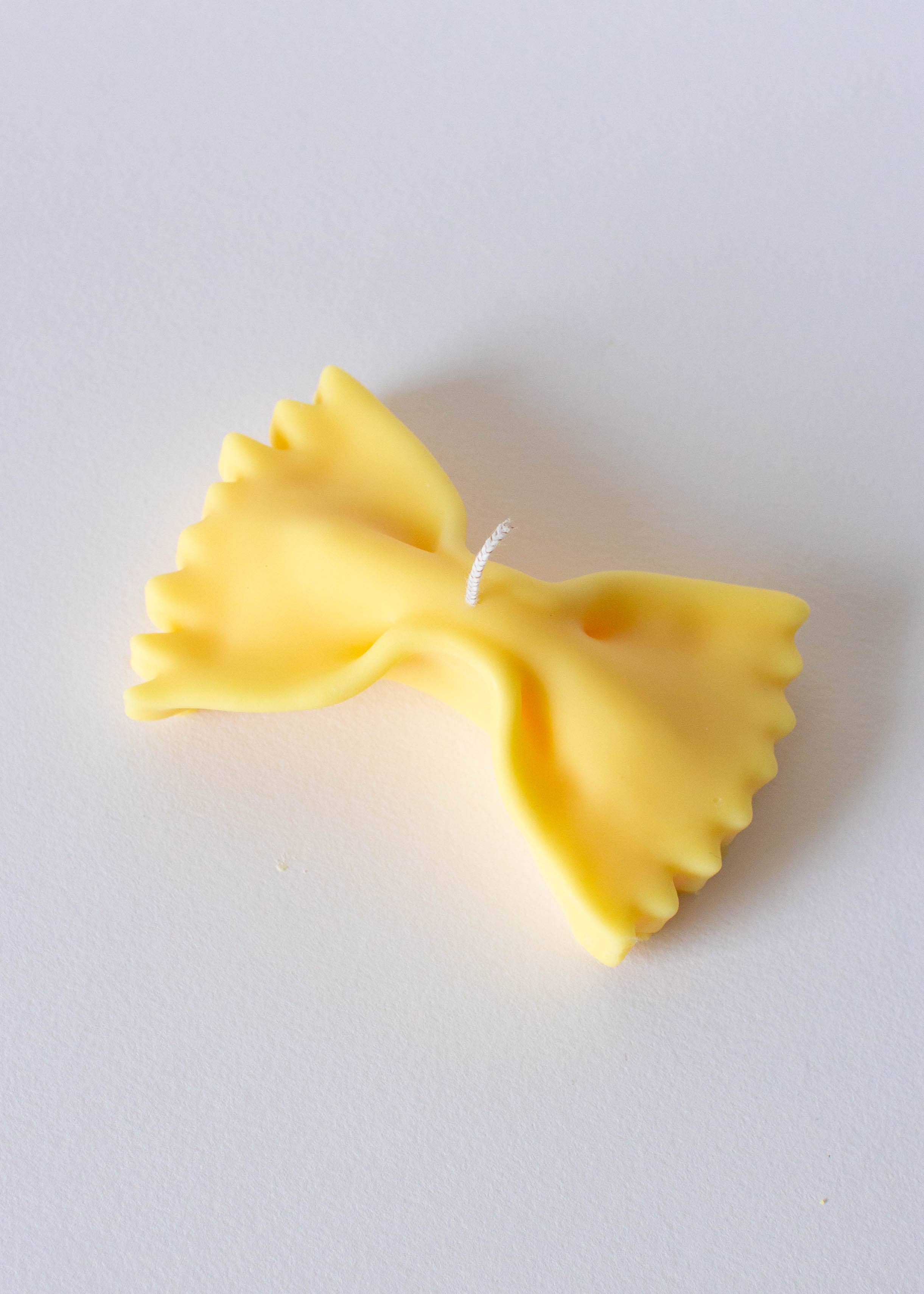 Yellow bow-shaped farfalle pasta candle on a white background.