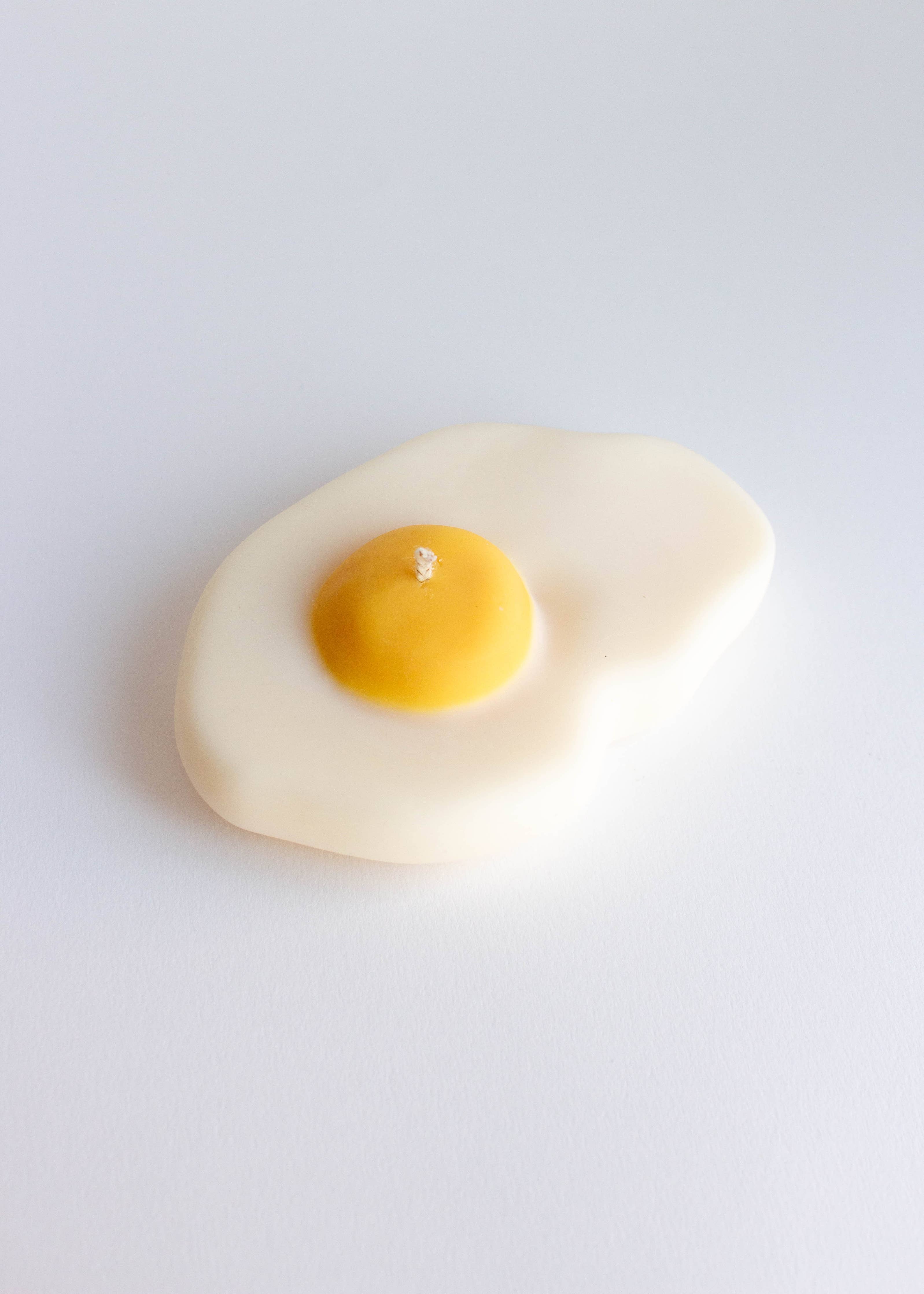 Candle shaped like a fried egg with a yellow center on a white background