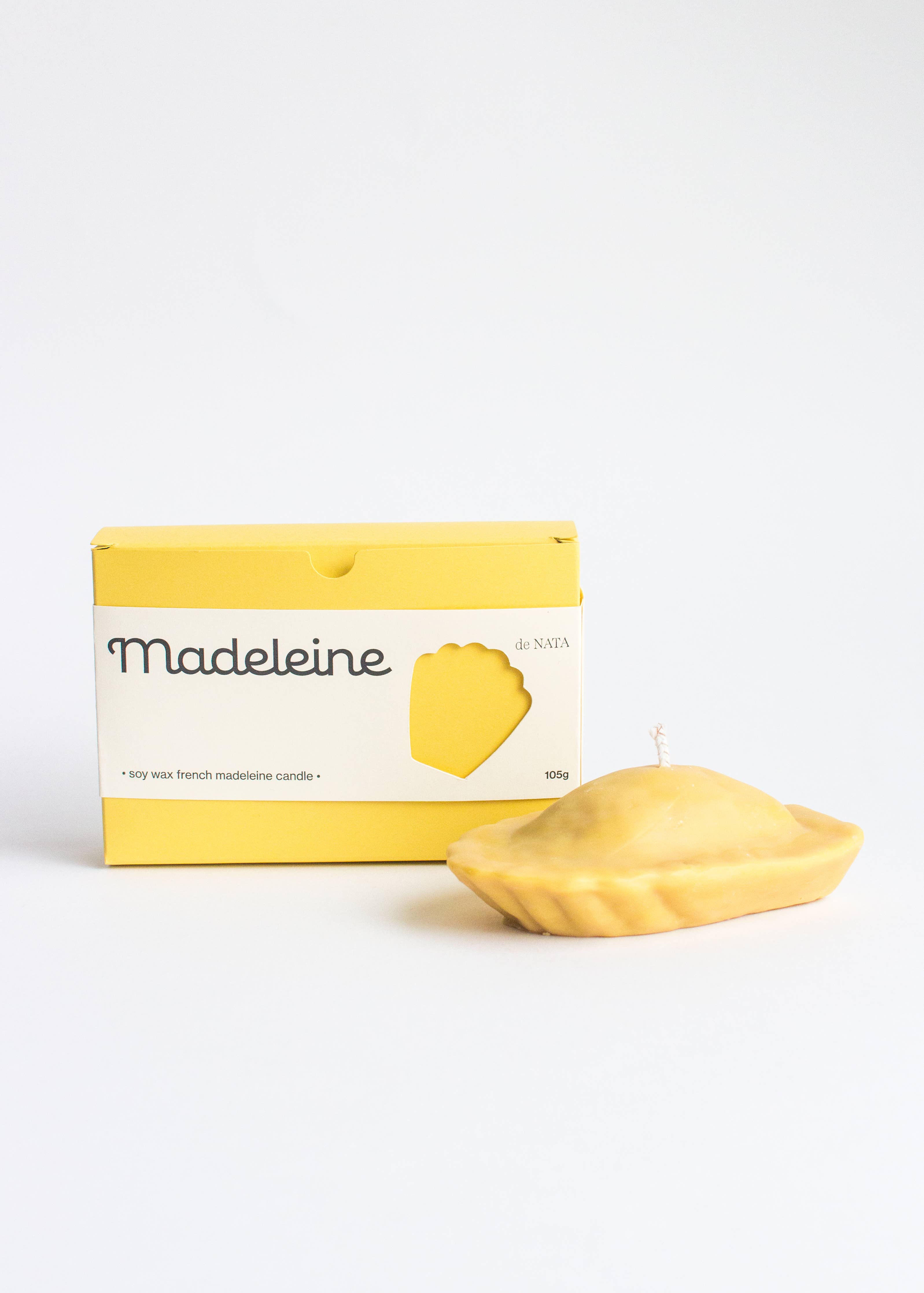 Yellow candle shaped like a Madeleine cake with 'Madeleine' packaging on a white background. Part of the Playful Food Candle Collection available via Wildschut Antiques Concept Store.