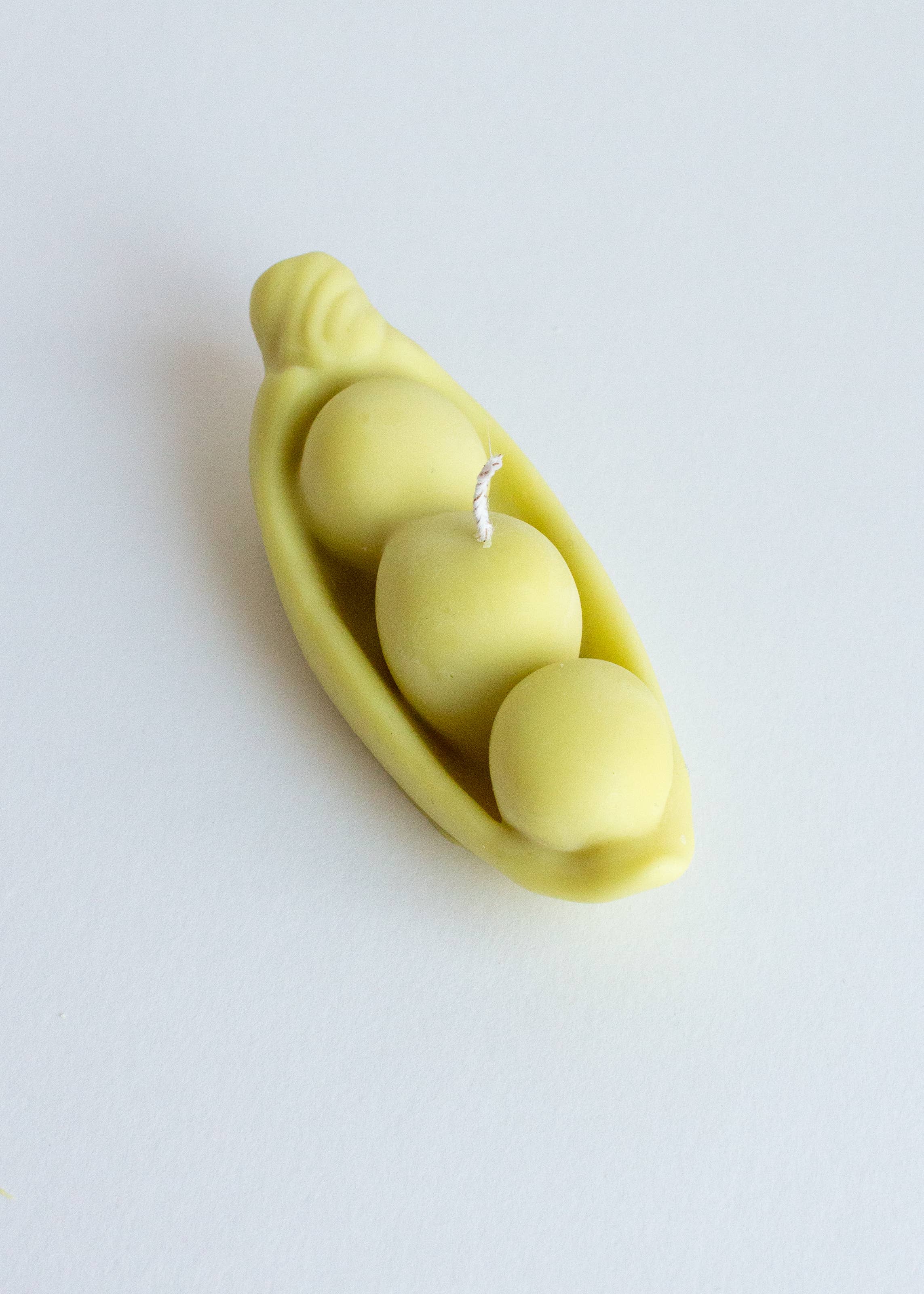Light green candle shaped like a pod with three peas on a white background. Part of the Playful Food Candle Collection available via Wildschut Antiques Concept Store