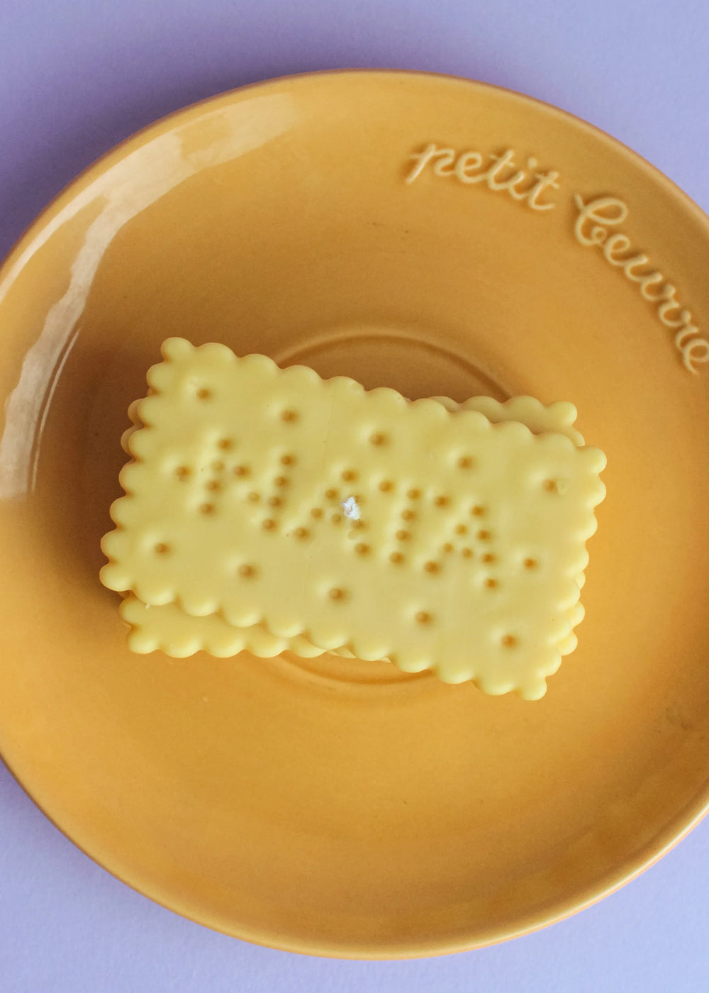 A biscuit-shaped candle on a brown plate against a light purple background