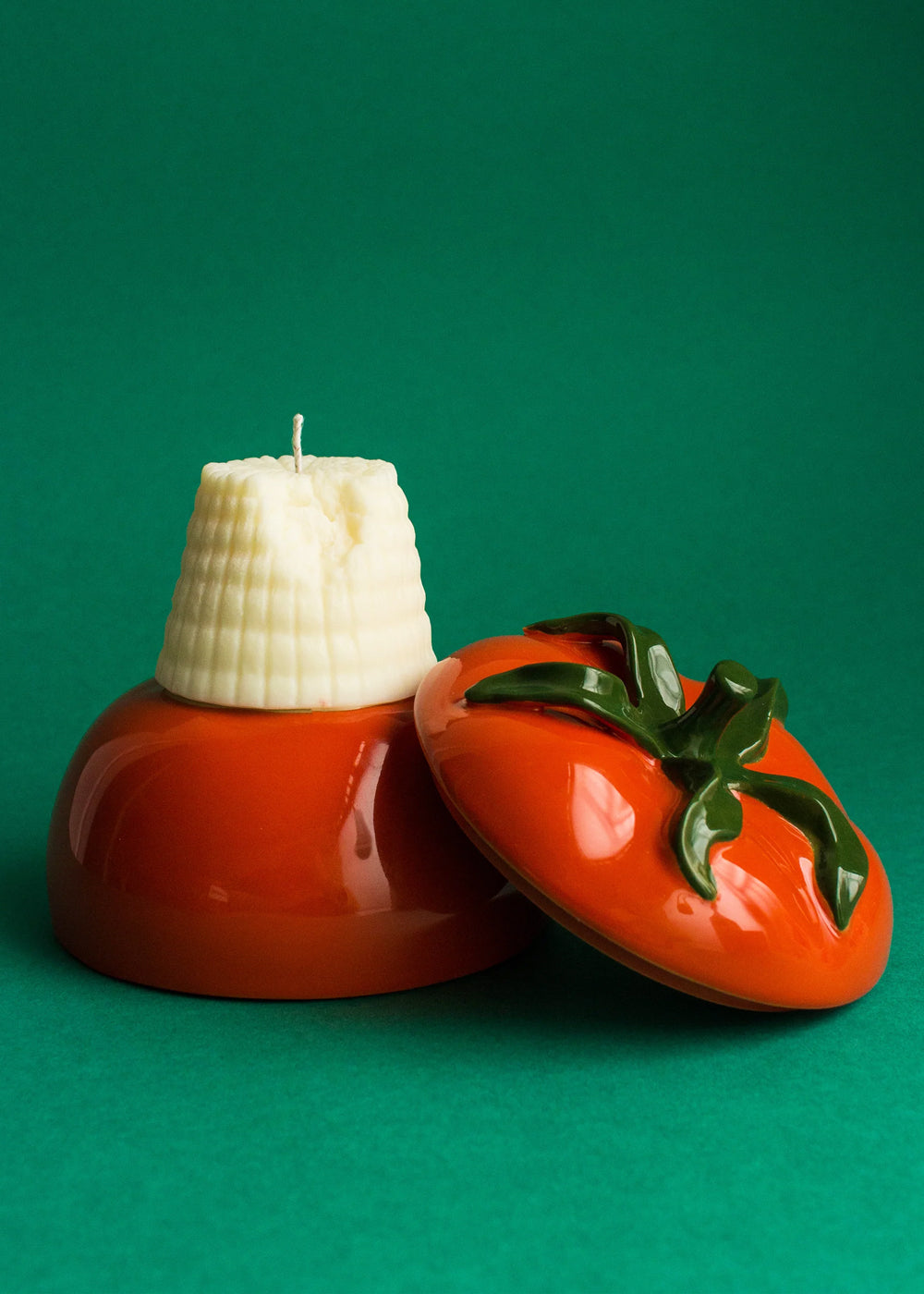 Ricotta cheese-shaped candle on a red tomato shaped holder on a green background