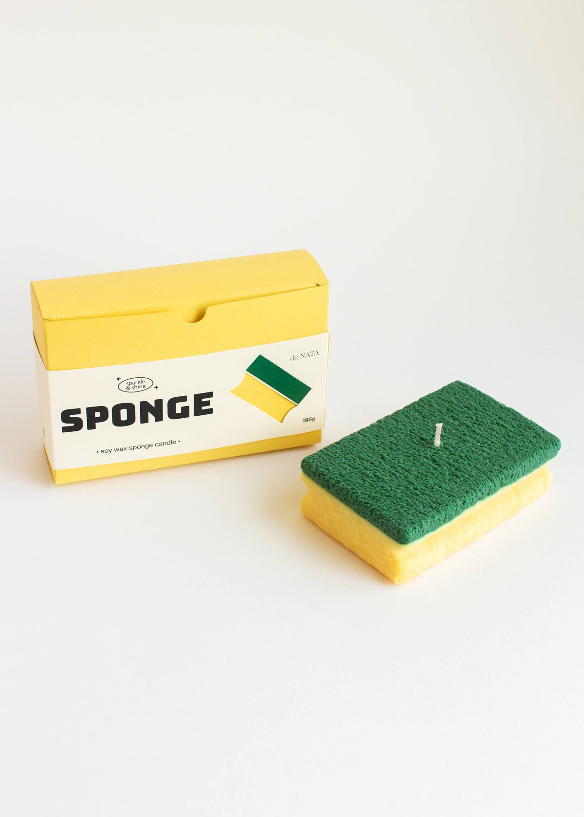 Green sponge with yellow handle next to its packaging on a white background. Fun fact, this sponge is a candle! Part of the Playful Food Candle Collection available at Wildschut Antiques Concept Store