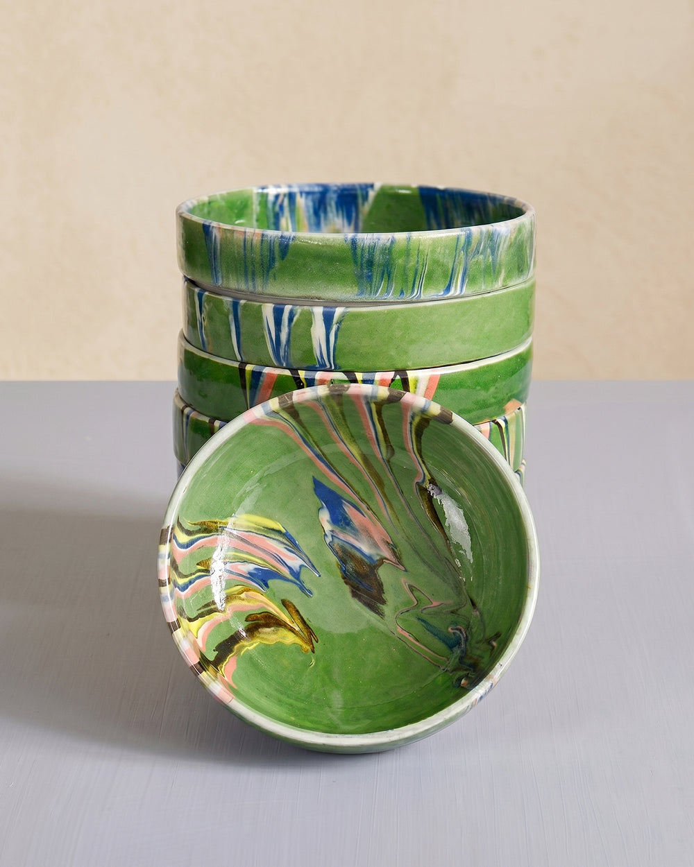 Stack of vintage green ceramic bowls with marble-pattern interior displayed on a grey surface, available at Wildschut Antiques.
