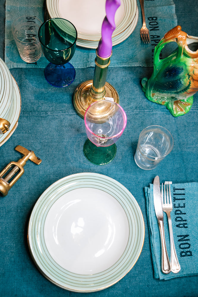 Colorful table setting with plates, cutlery, and decorative items on a teal blue tablecloth.
