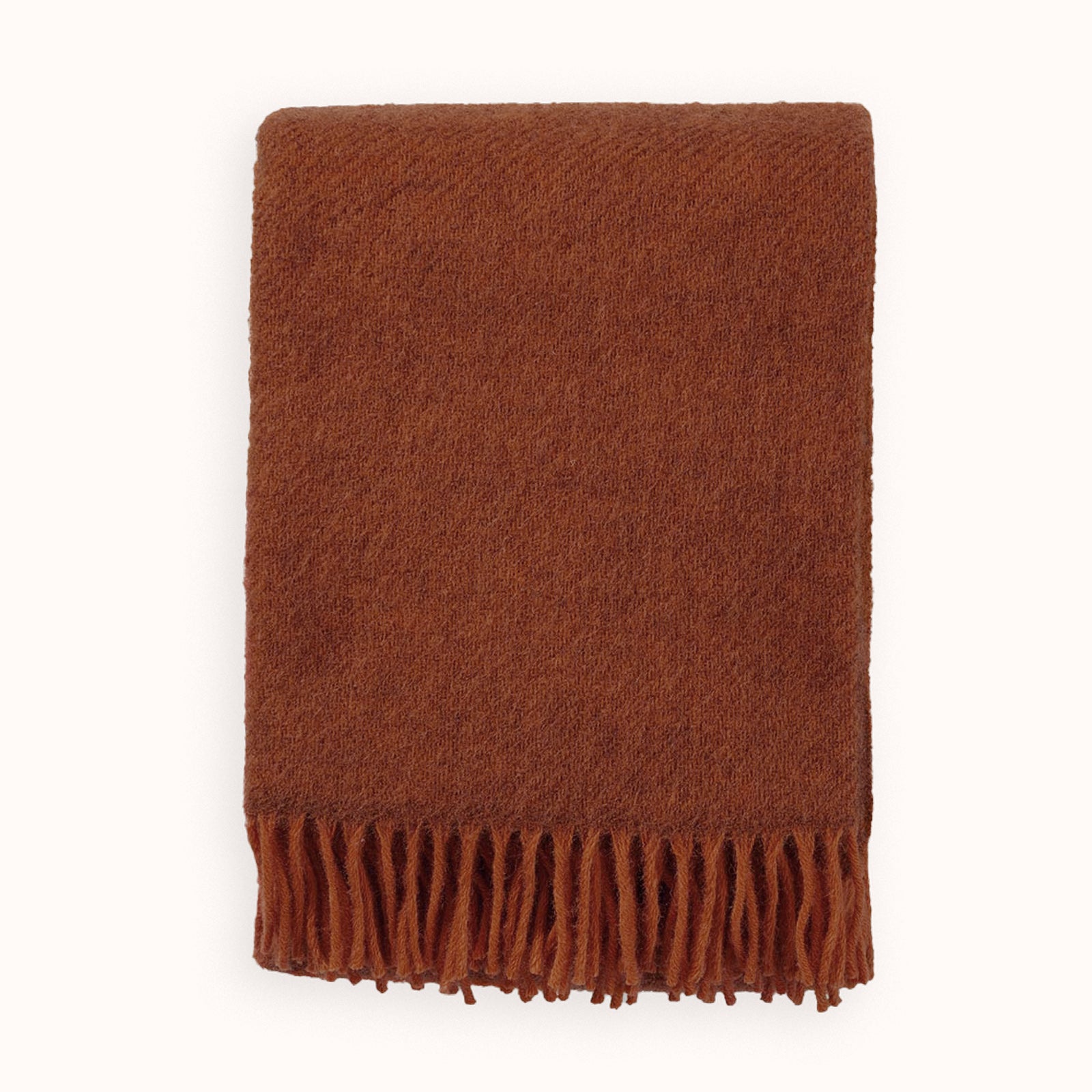 Neatly folded rust red brown coloured blanket with fringes on a white background by Klippan 1879, available at Wildschut Antiques.