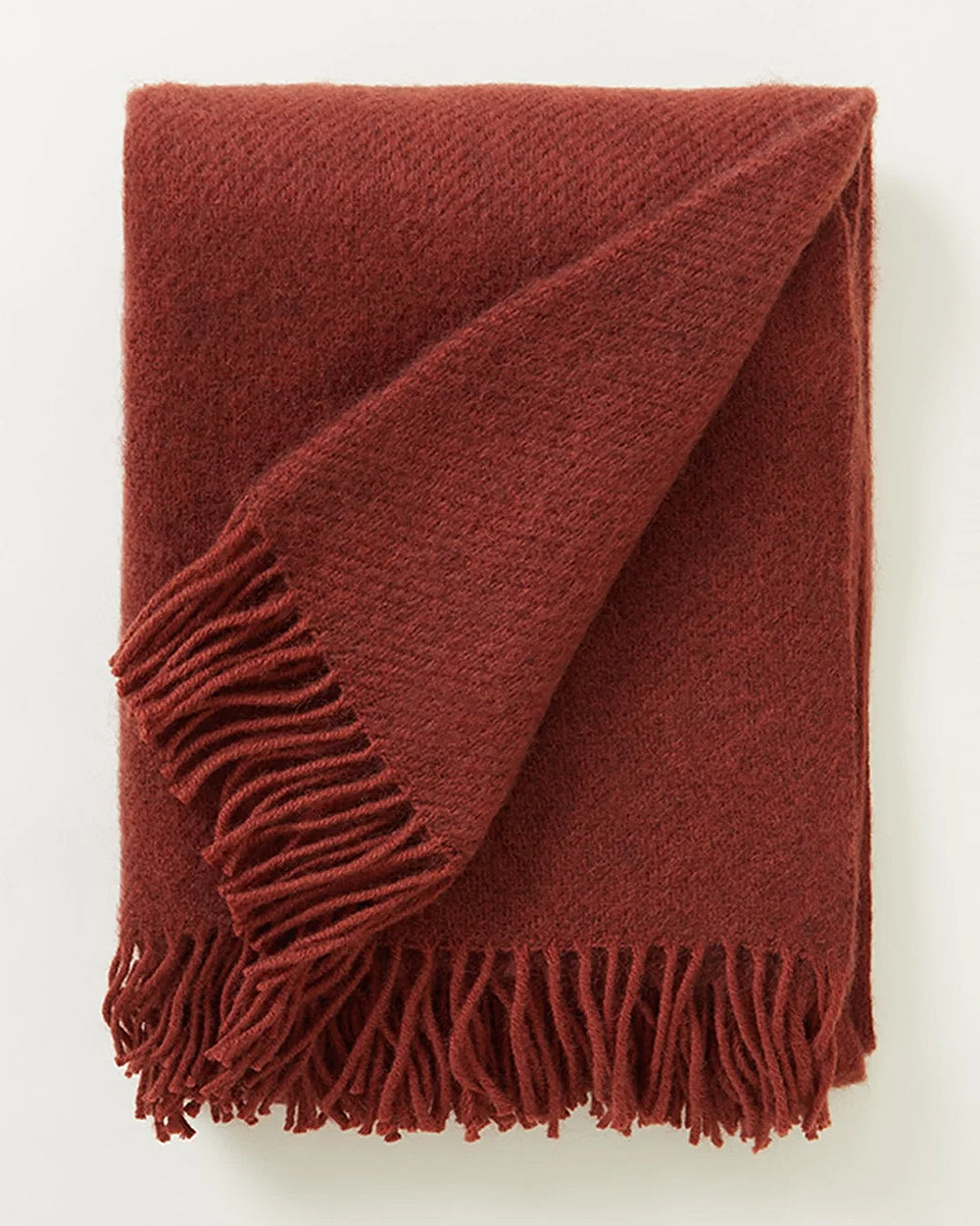 Neatly folded rust red brown coloured blanket with fringes on a white background by Klippan 1879, available at Wildschut Antiques.