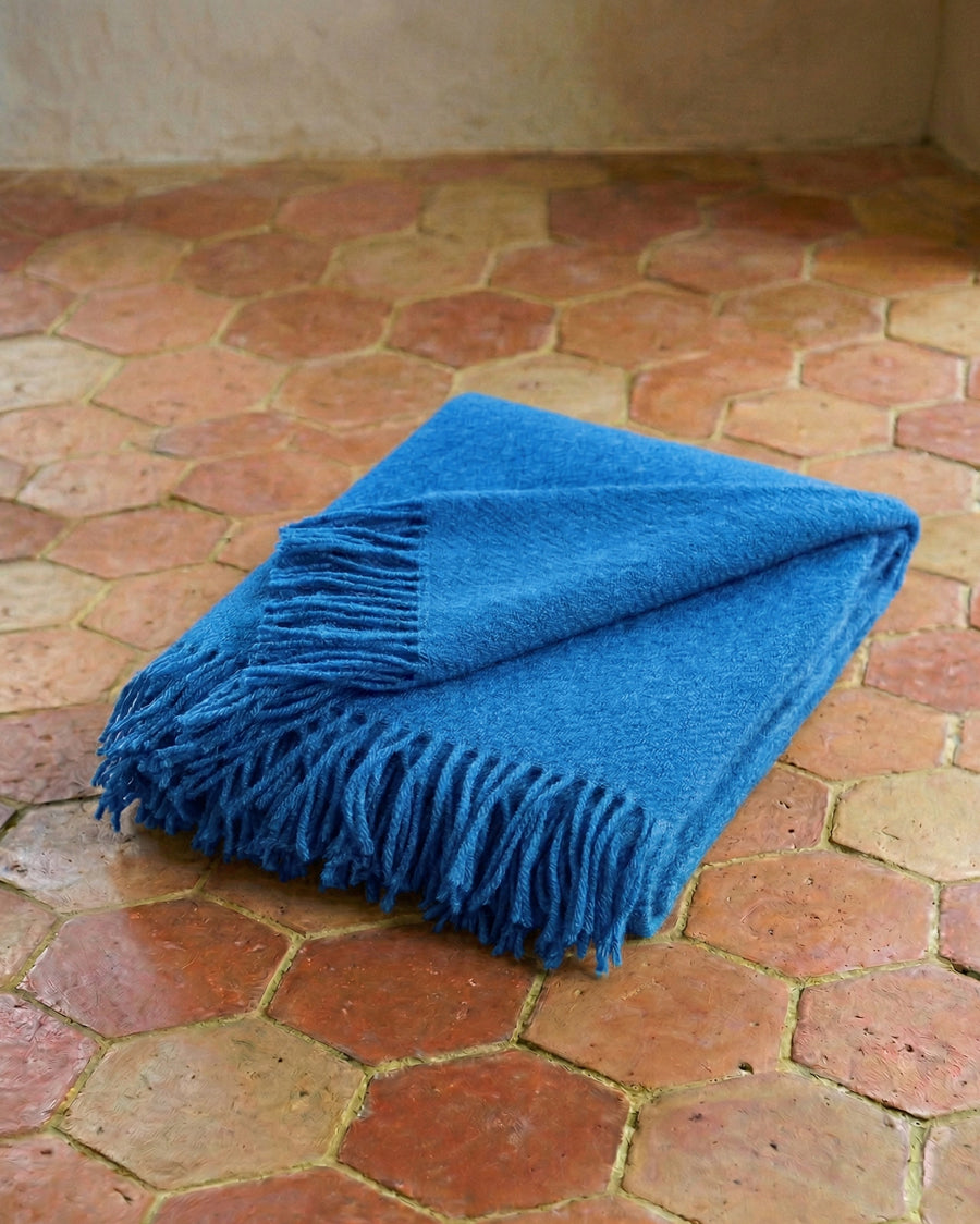 Cobalt blue wool throw blanket with fringes on a terracotta floor. By Klippan, available via Wildschut Antiques.