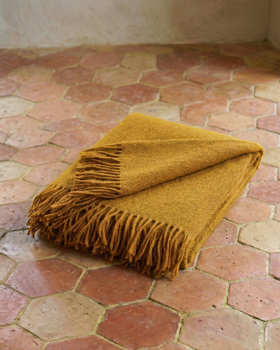 Mustard honey yellow wool blanket with fringes on a terracotta tiled floor. By Klippan, available via Wildschut Antiques.