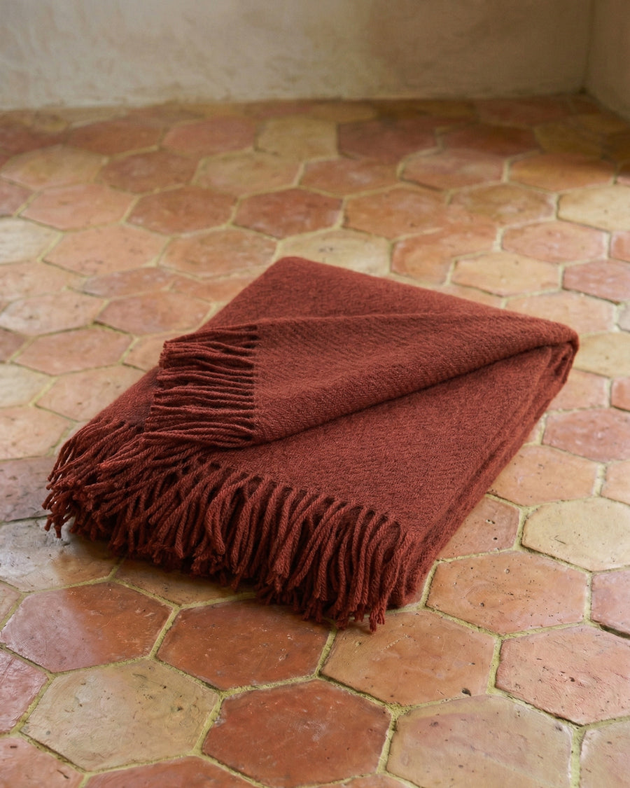 Rust brown wool throw blanket with fringes on a terracotta floor. By Klippan, available via Wildschut Antiques.