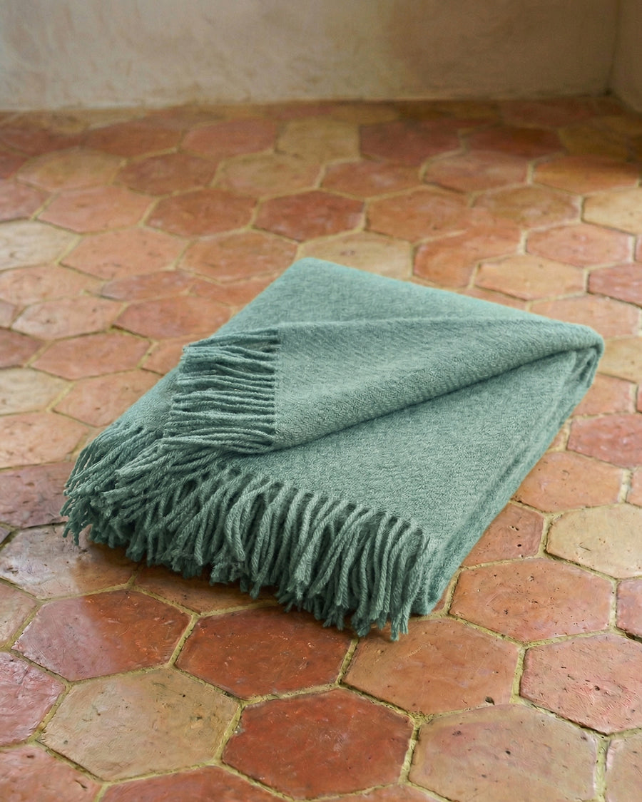 Turquoise wool throw blanket with fringes on a terracotta floor. By Klippan, available via Wildschut Antiques.