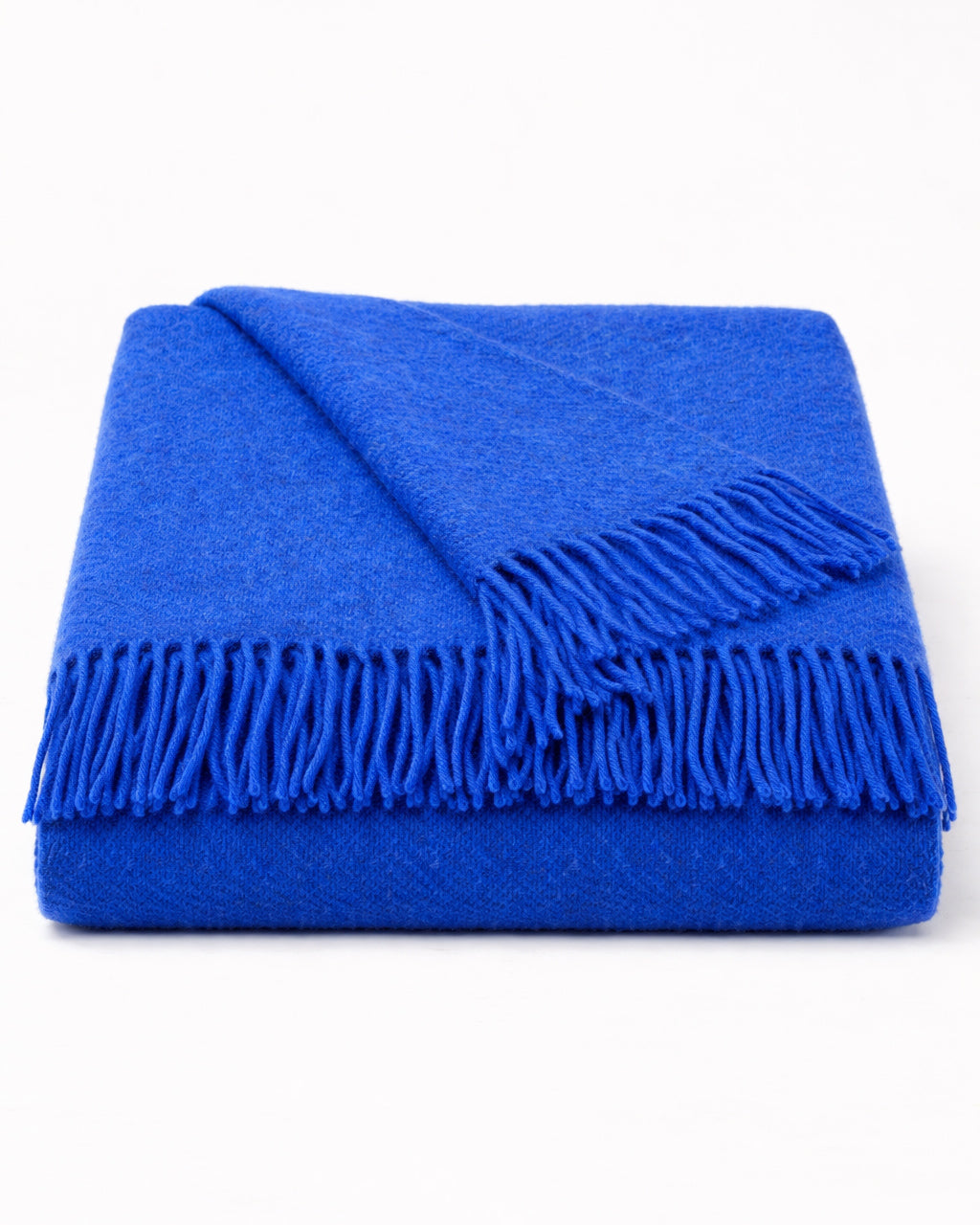 Neatly folded cobalt blue wool blanket with fringes on a white background, by Klippan 1879, available at Wildschut Antiques.