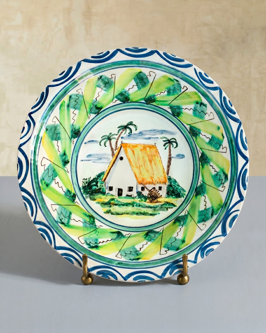 Large vintage Italian decorative ceramic bowl with a tropical scene and blue decorative border on a stand, displayed on a beige background, available at Wildschut Antiques.
