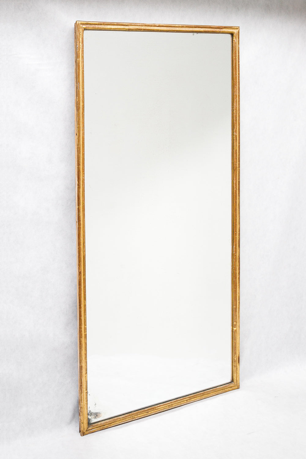 Sideview of a rectangular antique French mirror with a slender gold frame, set against a white background