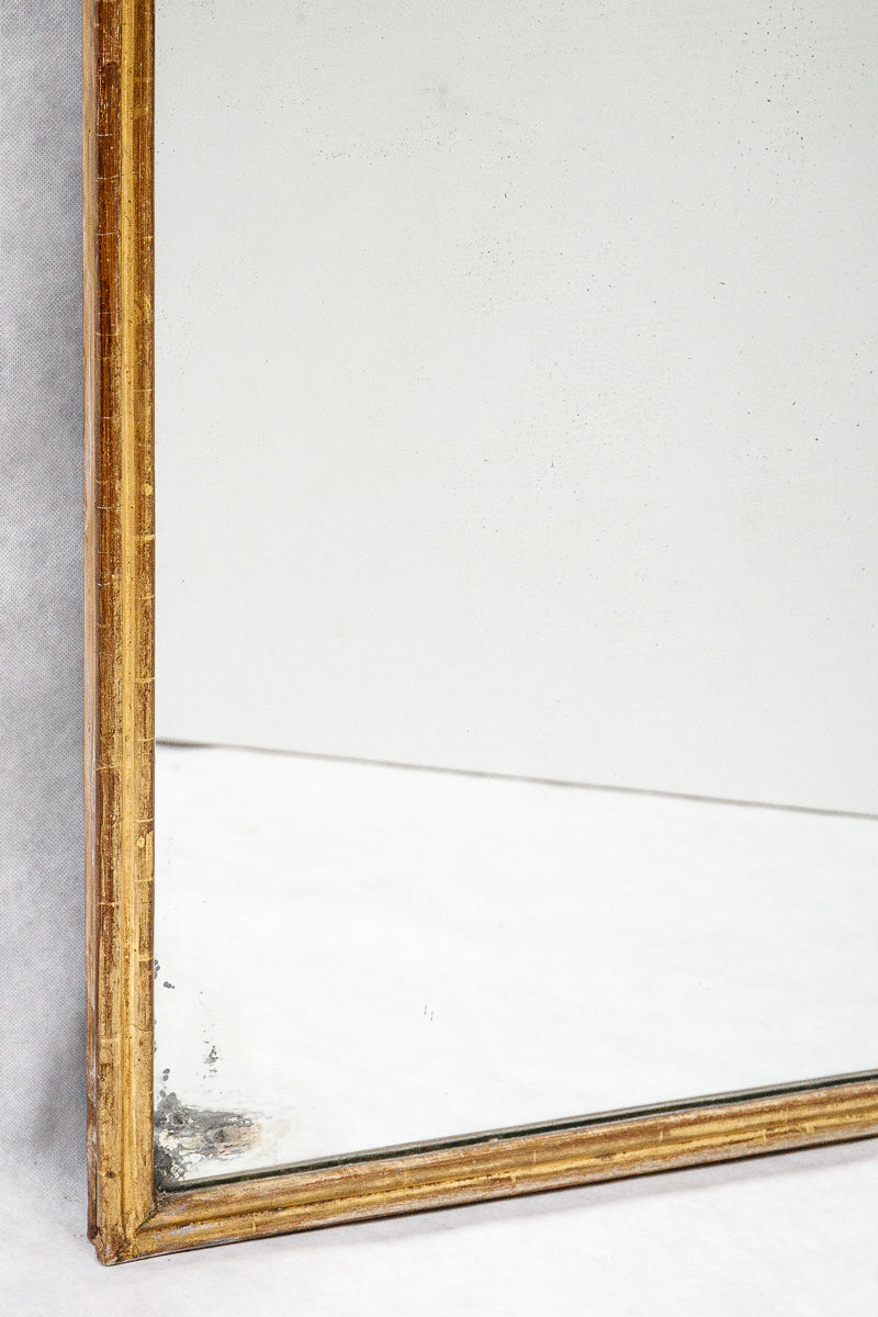 Close-up of a corner of a rectangular antique French mirror with a slender gold frame, showing some foxed patches