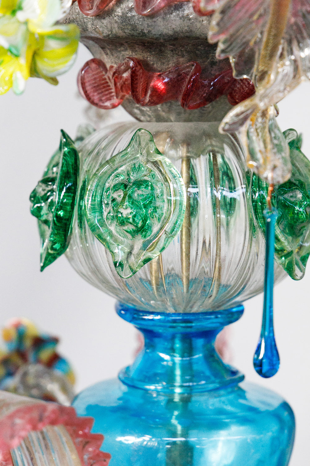 Close-up of a colorful vintage Venetian glass chandelier with intricate green lion head designs on a white background, available via Wildschut Antiques