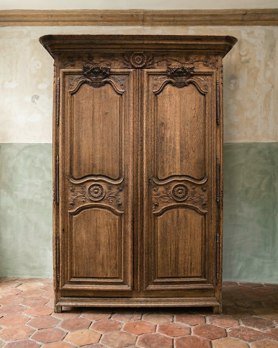 Antique French wooden marriage armoire with ornate carvings on a textured wall background, available via Wildschut Antiques.