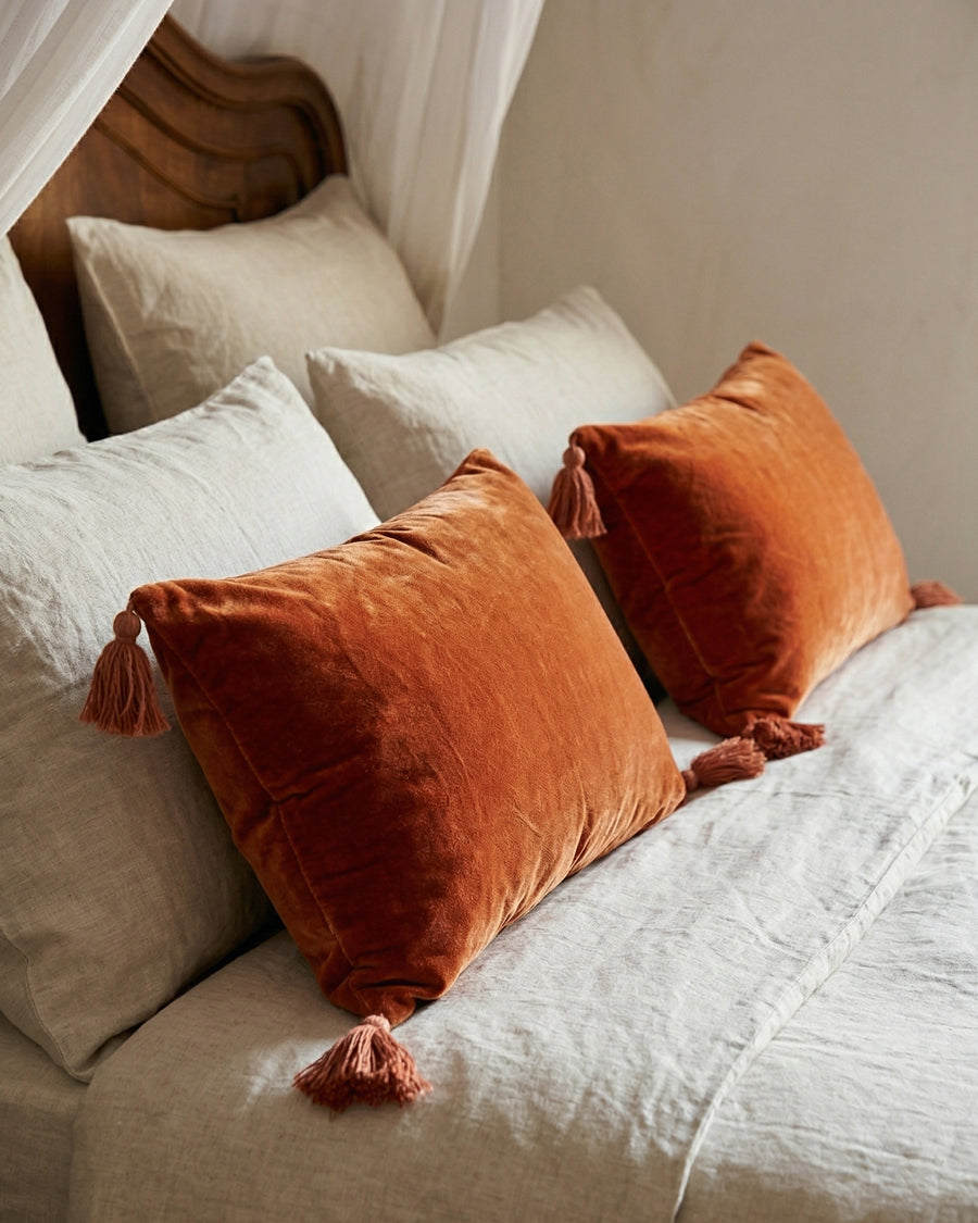 Orange-red velvet pillows with tassels on a bed with white bedding, by Monde Sauvage available via Wildschut Antiques.