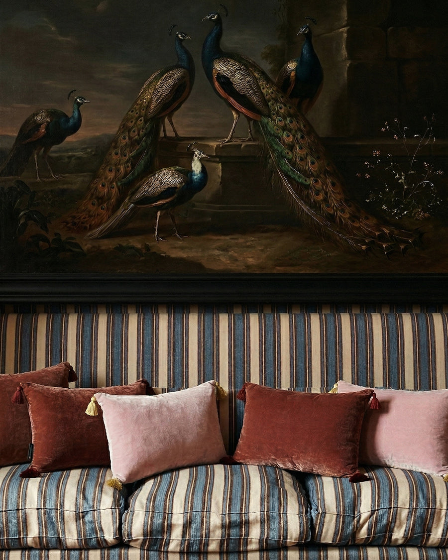Striped sofa with colorful velvet pillows in front of a painting of peacocks, by Monde Sauvage available via Wildschut Antiques.
