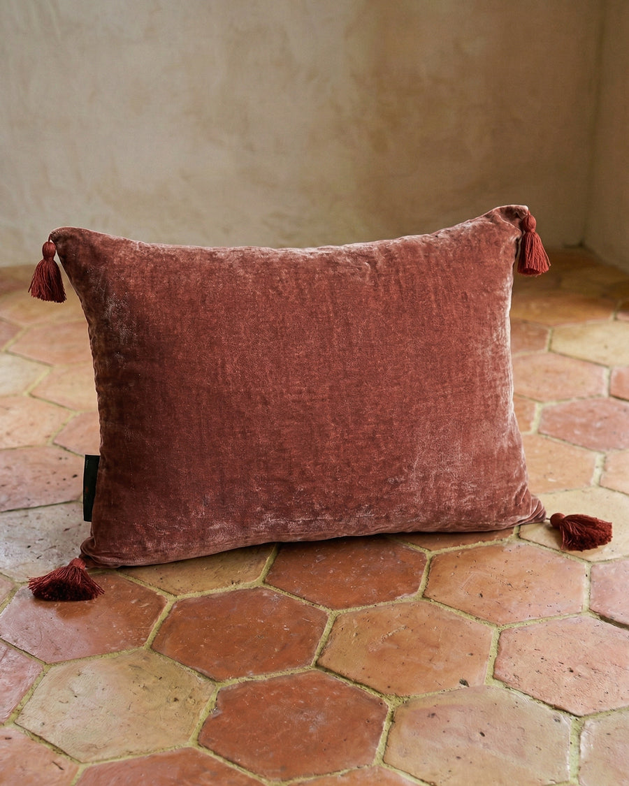 Dark peach velvet pillow with yellow tassels on a terracotta floor. By Monde Sauvage, available via Wildschut Antiques.
