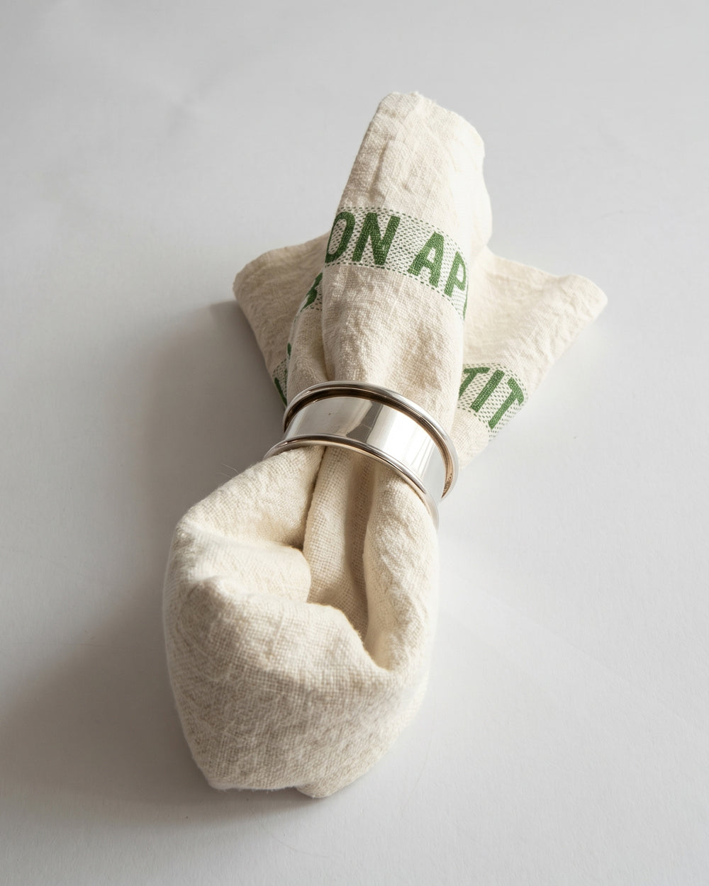 Folded ecru linen napkin with a silver ring on a light gray background