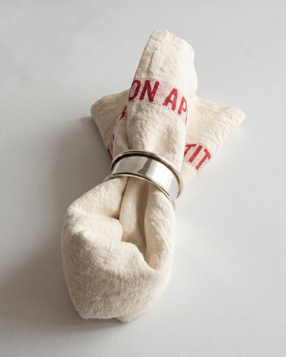 Folded linen napkin with a silver ring on a white background. 