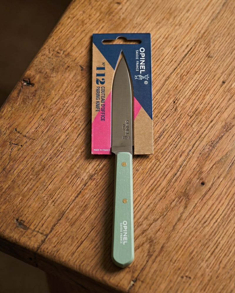 Opinel kitchen knife with sage green handle and silver blade, photographed on a wooden table top, part of the kitchenware collection available at Wildschut Antiques.
