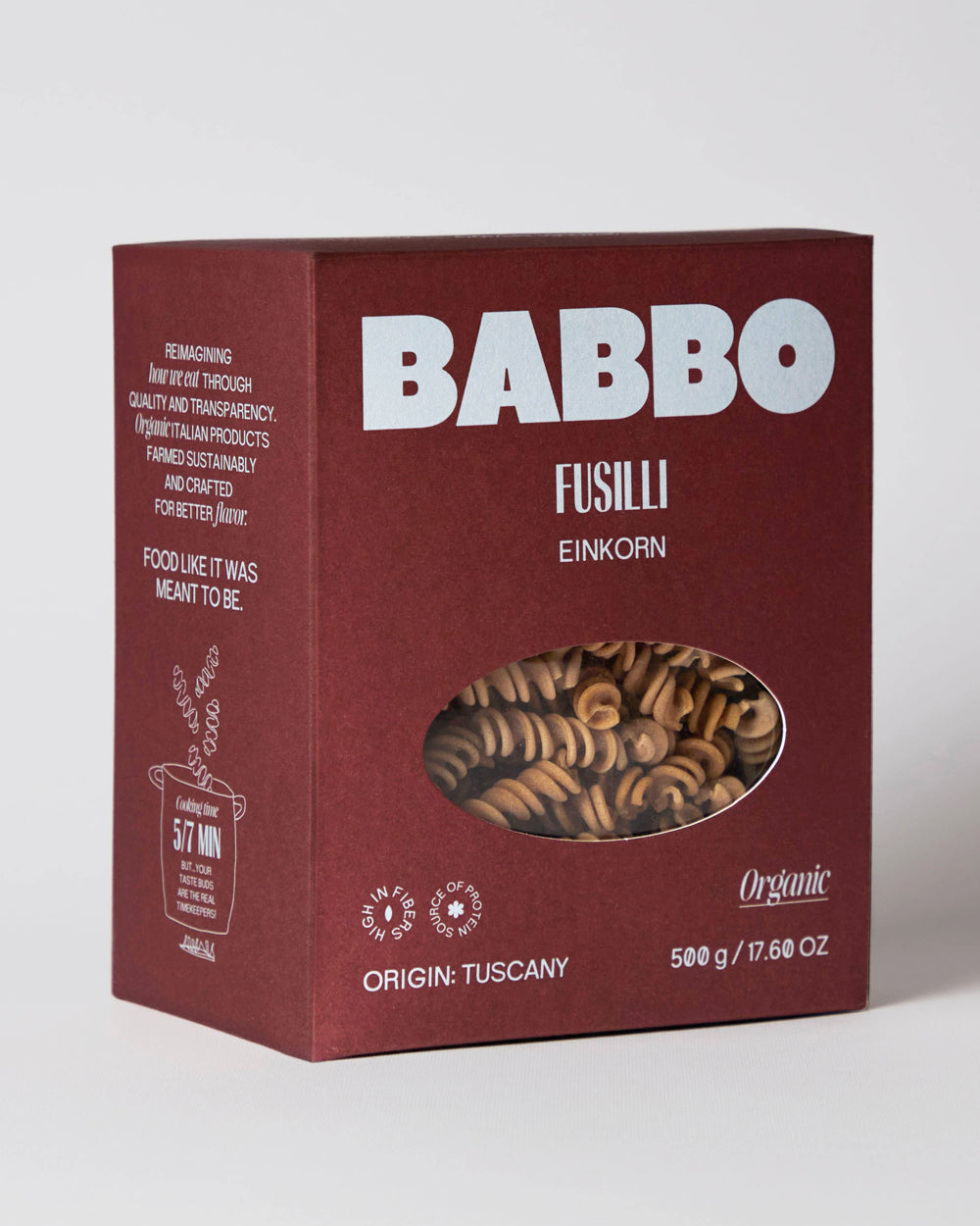 A box of Babbo Fusilli Einkorn pasta, featuring a deep burgundy packaging with white text and a clear oval window showing the spiral pasta inside, set against a neutral light gray background. Available via the Pantry Collection from Wildschut Antiques.