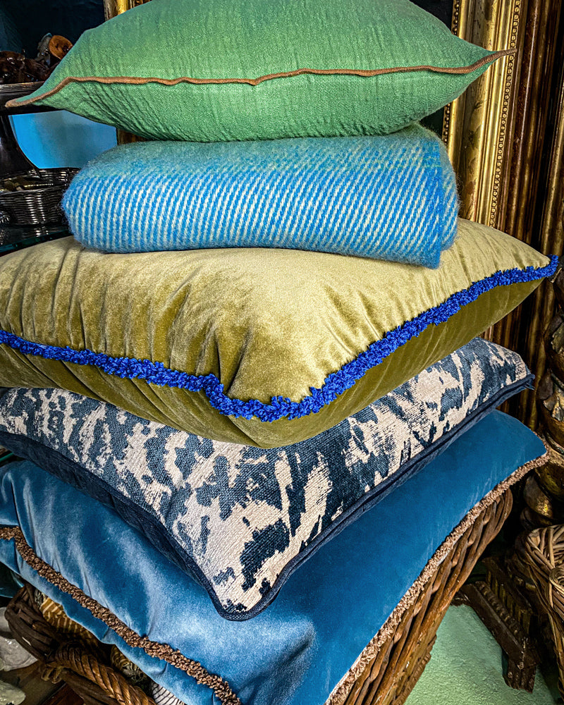 Stack of decorative pillows with various patterns and colors on a textured surface, available via Wildschut Antiques