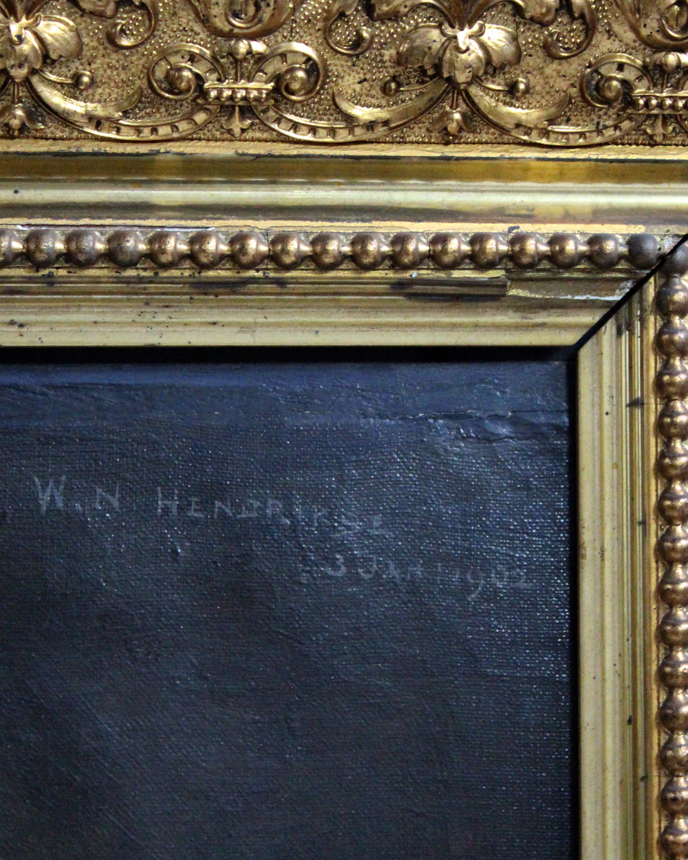 Close-up of an ornate gold and beige picture frame with a dark blue textured canvas or print filling most of the visible area. Faint handwritten text appears on the dark surface.
