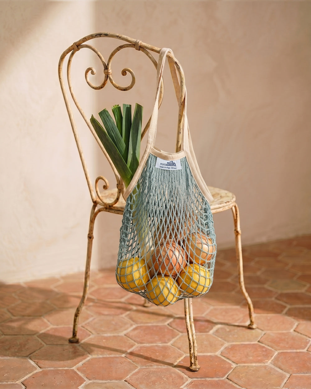 Light blue shopping net with fruits and vegetables on a decorative vintage French metal chair.  By Filt 1860, available at Wildschut Antiques.