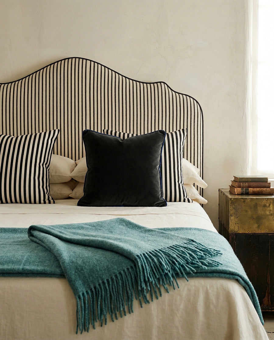 Bed with striped headboard, striped pillows, dark green velvet pillow, and turquoise wool blanket in a bedroom setting. Items via Wildschut Antiques.