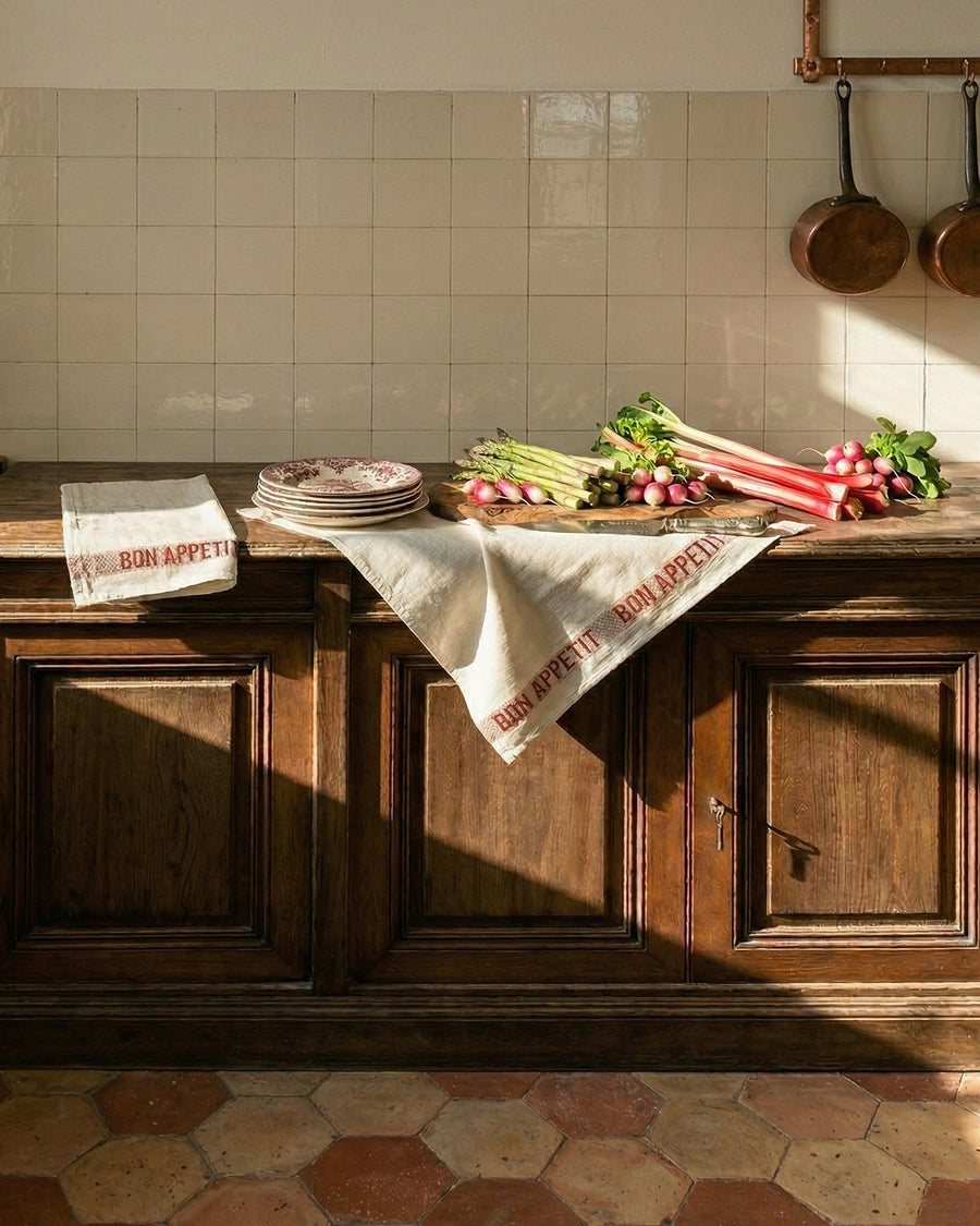 Wooden kitchen counter with vegetables and 'Bon Appetit' towels, tiled wall in the background, by Charvet Editions available via Wildschut Antiques.