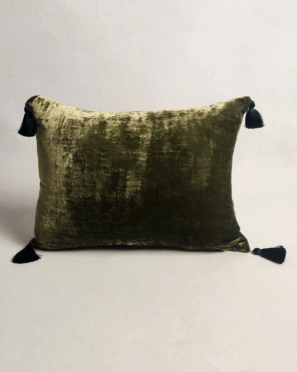 Olive green silk velvet velour pillow with contrasting pom-pom tassel details on a light grey background. Designed by Monde Sauvage Paris, available at Wildschut Antiques.
