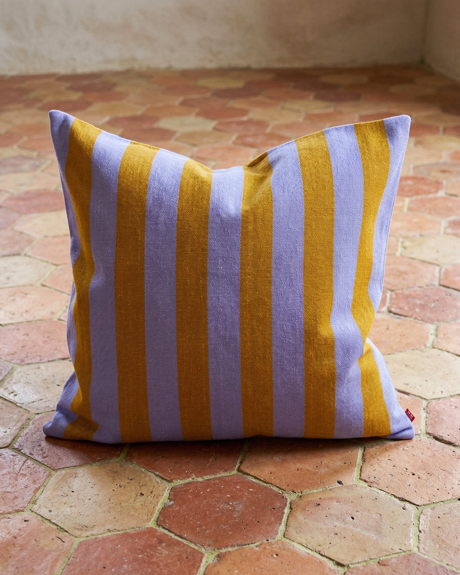 Striped pillow with yellow and purple stripes on a terracotta floor.