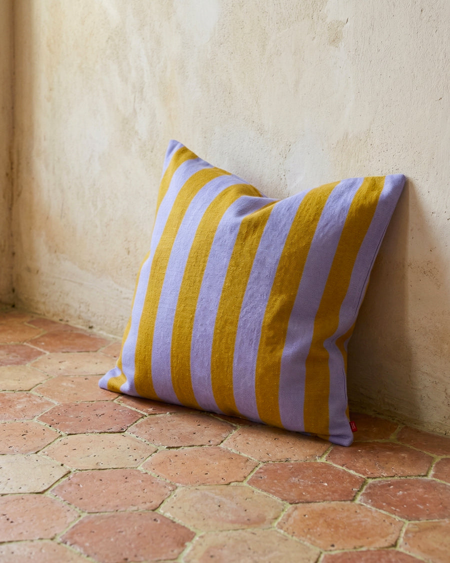 Striped yellow and purple pillow on a terracotta floor against a beige wall