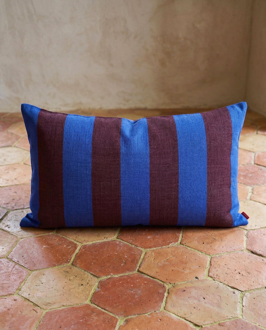 Striped blue and brown pillow on a terracotta floor, available via Wildschut Antiques.
