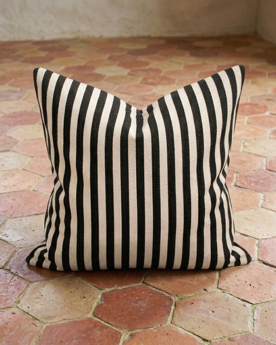 Black and white striped pillow on a terracotta tiled floor, available via Wildschut Antiques.